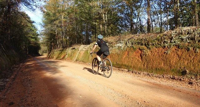a cyclist rides on a red dirt road