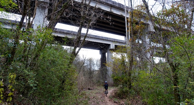 A cyclist rides a trail under a massive overpass
