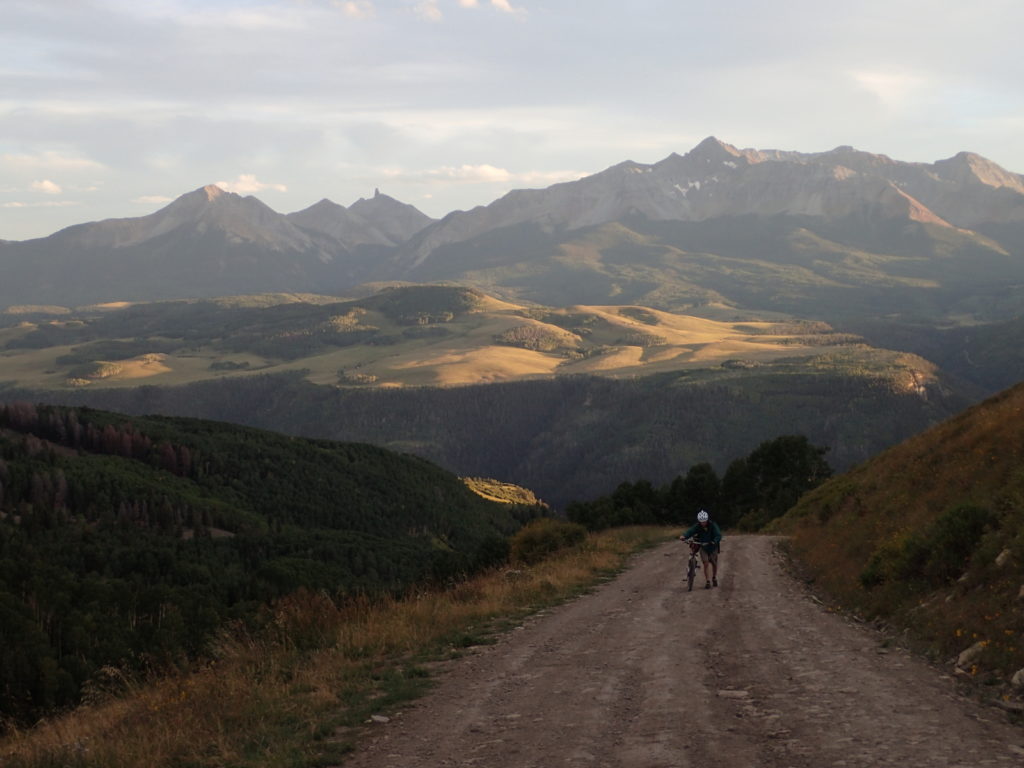 a lone cyclist pushes his bike up a steel moutain road