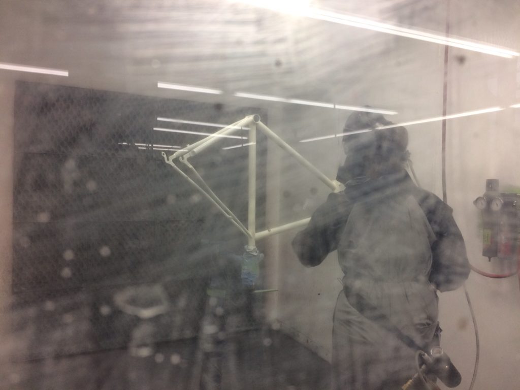 A painter sprays a bicycle frame inside a booth