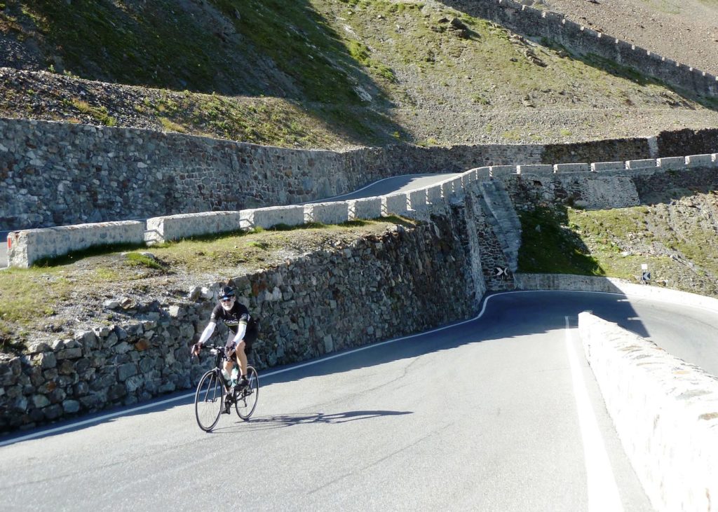 a cyclist climbs past a hairpin turn on a steel mountain road