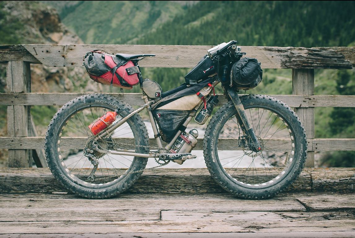 Joe's Seven Treeline SL, loaded to the gills for a bikepacking adventure, leans against a wooden bridge wall