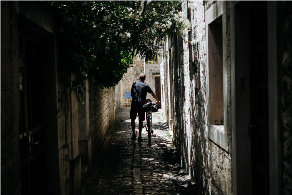 A cyclist walks his bike up a shady cobblestone street