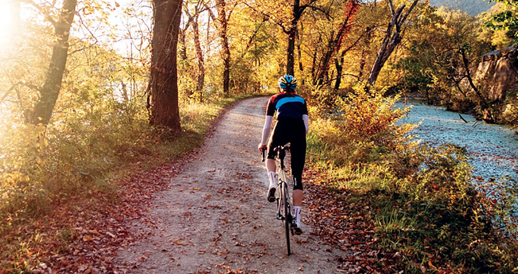 solo rider on a leaf-speckled path by a srteam on a New England autumn morning