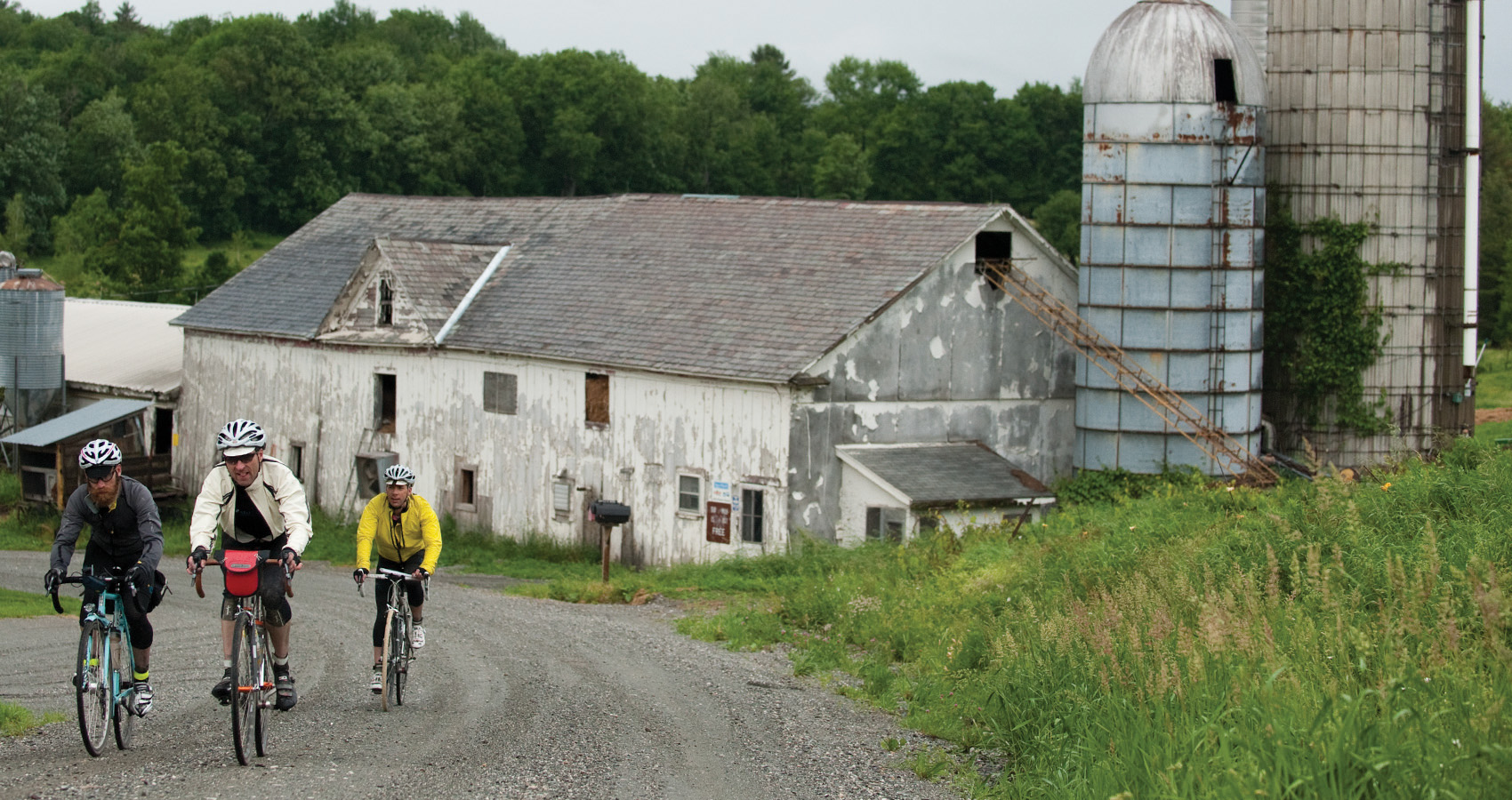 three riders pass a quaint farm in Vermont on a gravel road